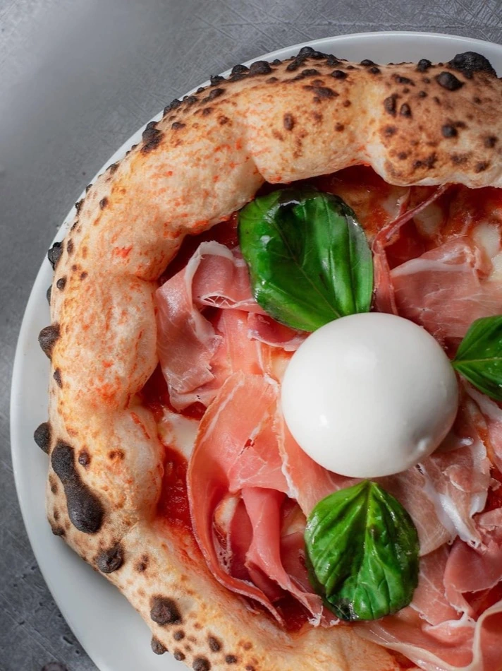 Prosciutto, burrata and basil pizza with a tall Neapolitan cornicione