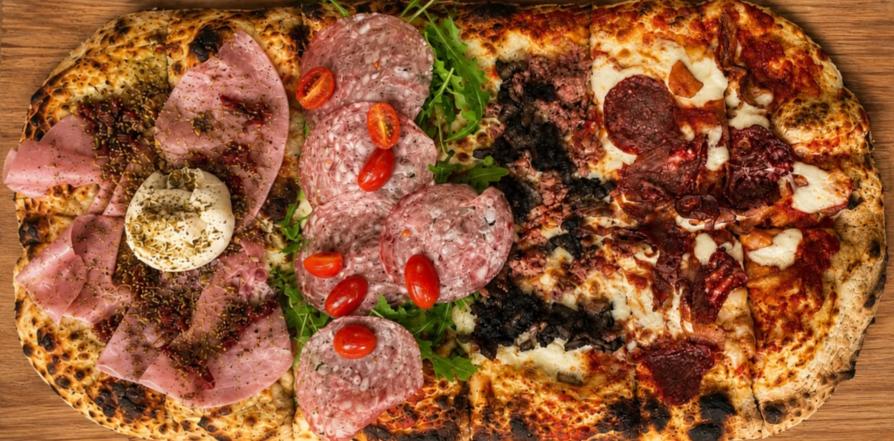 Pizza al metro seen from above: four toppings along one long Neapolitan base on a wooden board